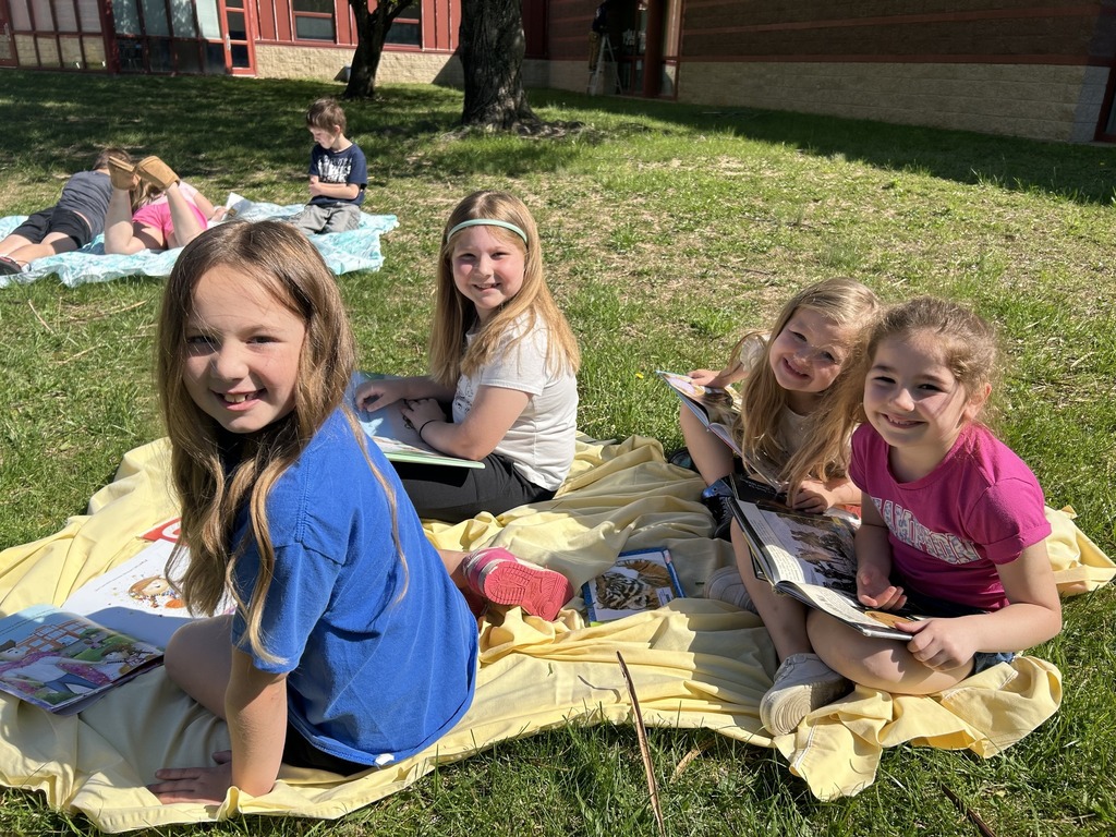 image shows children smiling as they read outside on a beautiful day