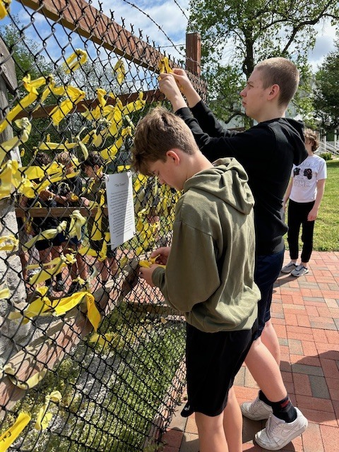 imnage shows a junior high school student tying a yellow ribbon at the guard tower outside of the pow/mia museum at jefferson barracks. 