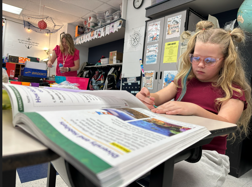 a student is seen drawing on a piece of paper while she also studies about animal habitats.
