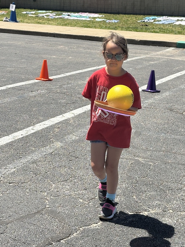 image is of a student running and balancing a ball on a frisbee during field day at the primary