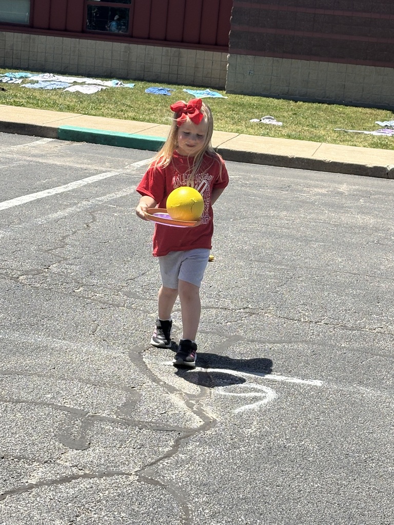 image is of a student running and balancing a ball on a frisbee during field day at the primary