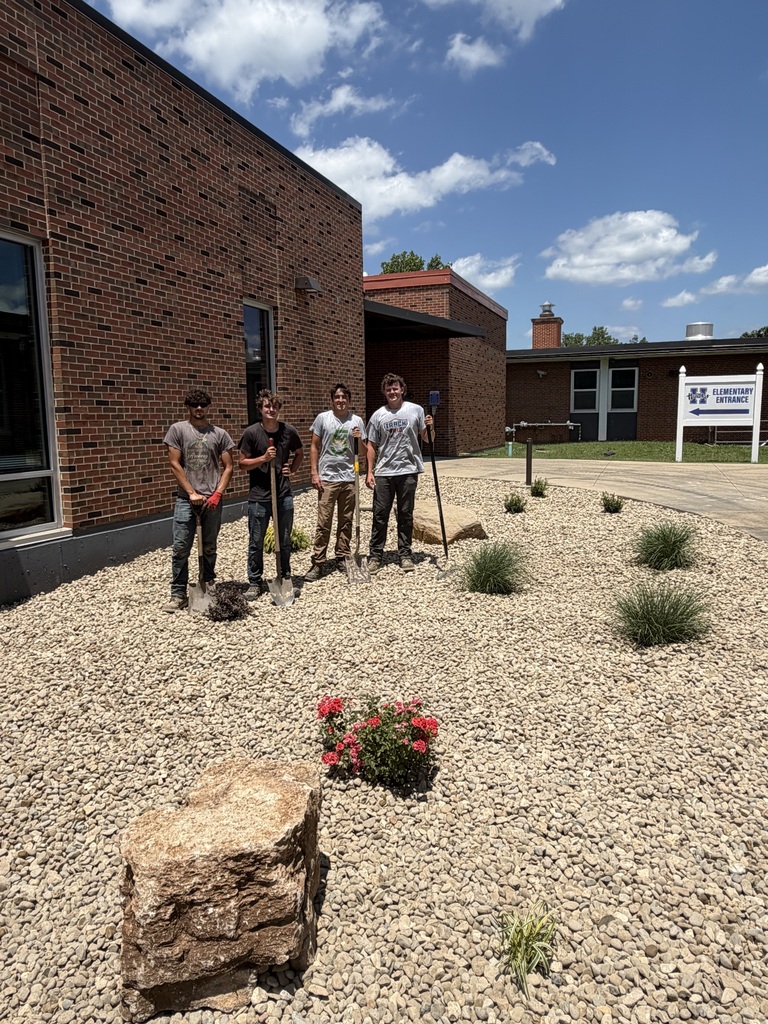 Mower Crew standing with several new plants, "planted" outside of the front entrance to Hillsboro Elementary School