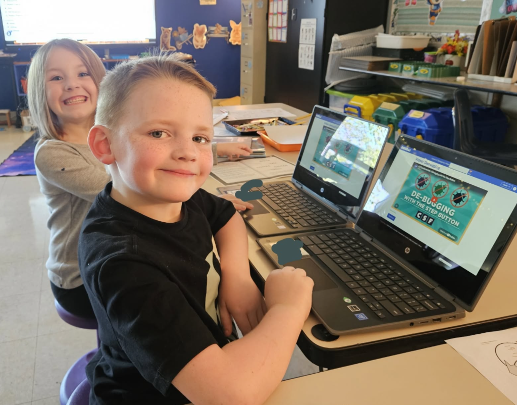 students sitting at laptops and smiling at the camera.