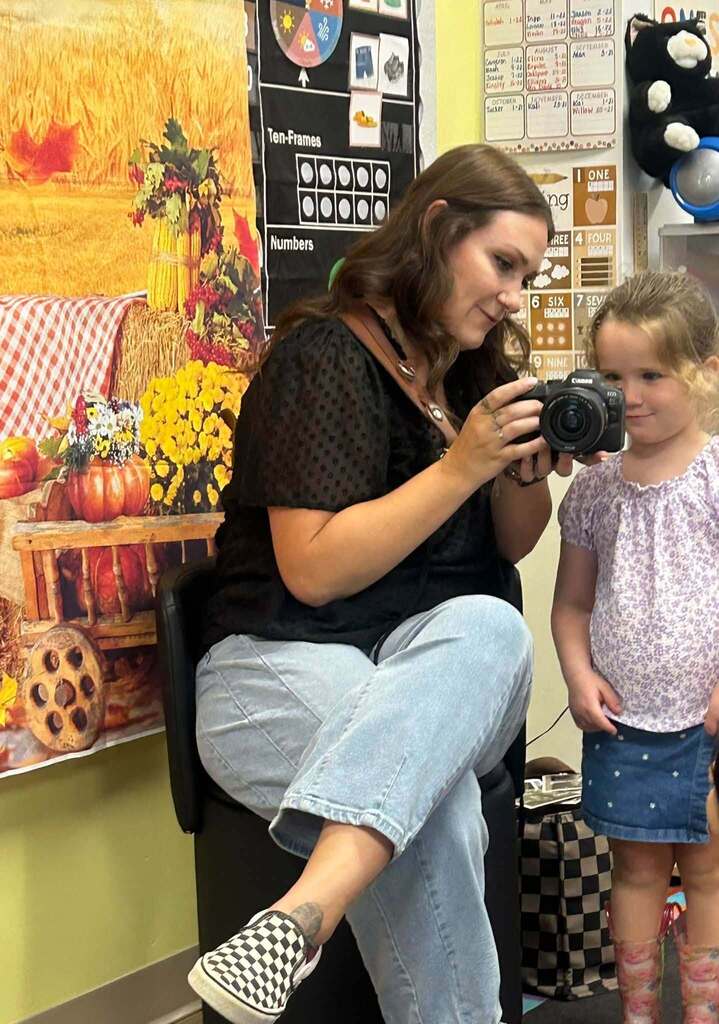 woman holds a camera while a woman looks into the lens.