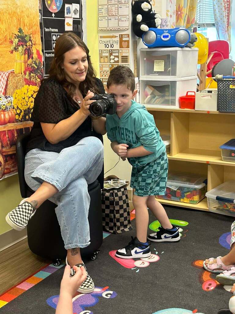 woman holds a camera while a student looks into the lens.
