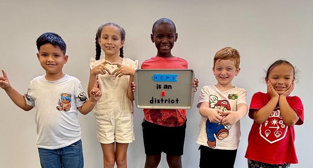 Elementary students smiling and holding up a sign that reads "HCPS is an A district"