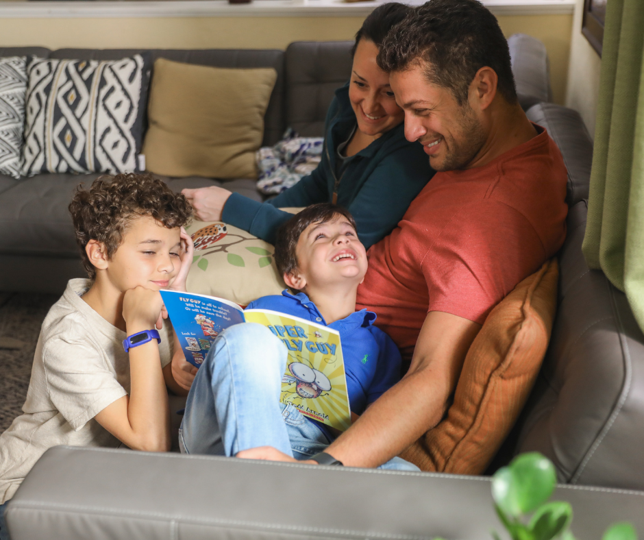 A mom and dad reading with their 2 sons on the couch.