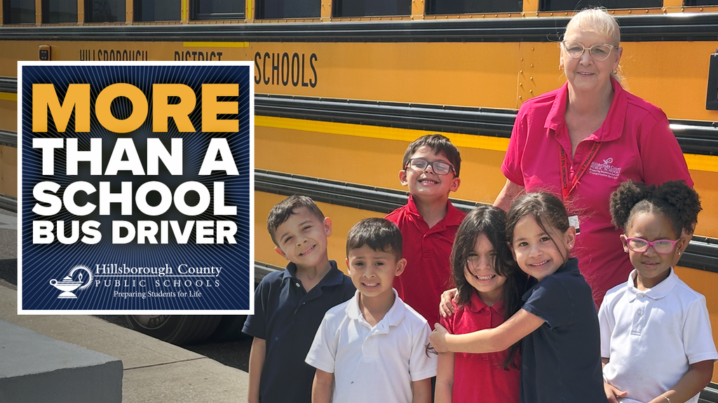 A female bus driver wearing a red shirt standing with a group of students in front of a school bus.