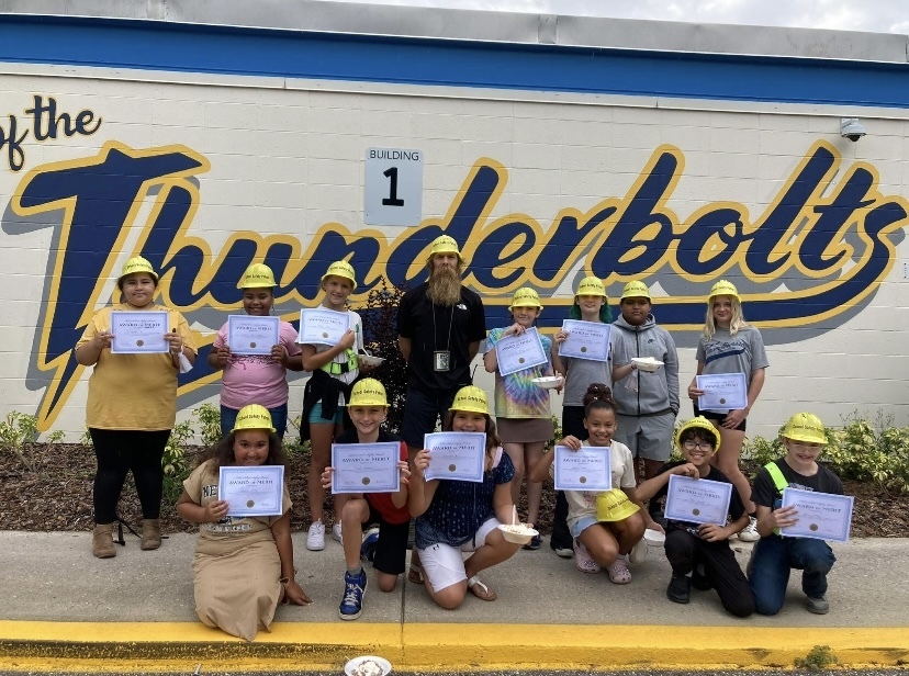 Safety Patrols are proudly holding up their certificates in front of the school.