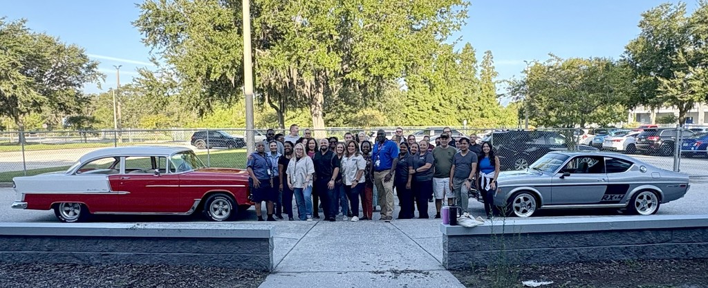 Staff poses between classic cars. 
