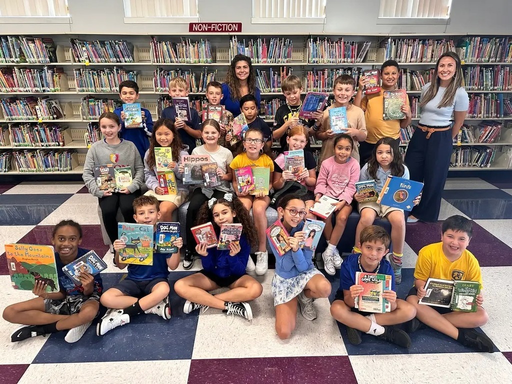 Class holding up the books they checked out of the library. 