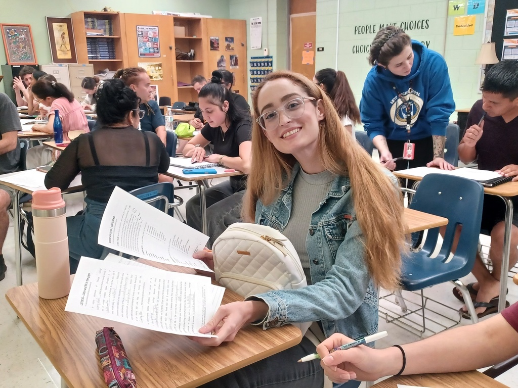 a student showing off her writing while others in the background  talk about their writing with their classmates