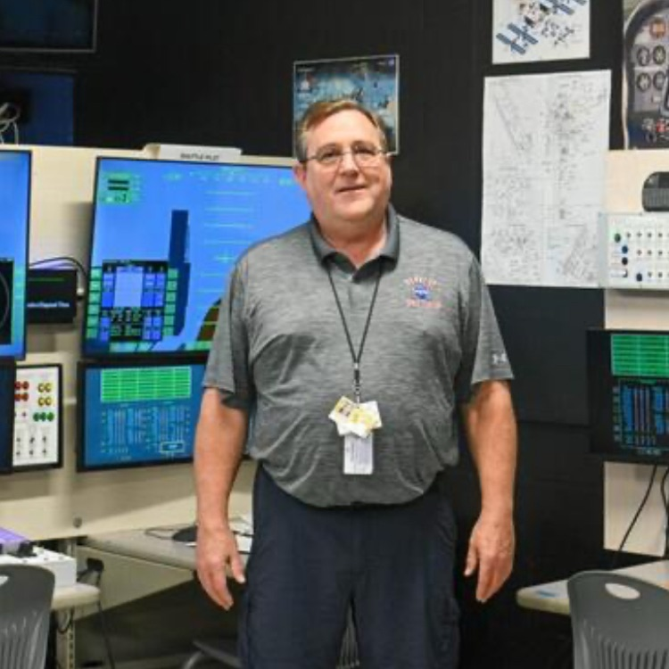 Teacher Brainard Harris in front of Shuttle simulator  
