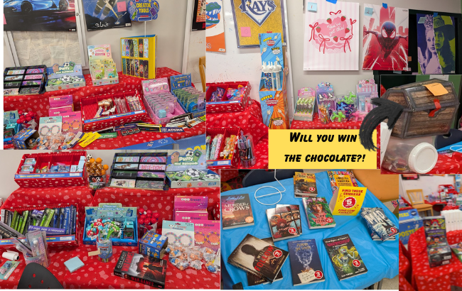 tables with red tablecloths covered with books, toys, and stationery, cardboard treasure chest on top of an opaque container of chocolate with a white lid; table with blue tablecloth with books on special sale