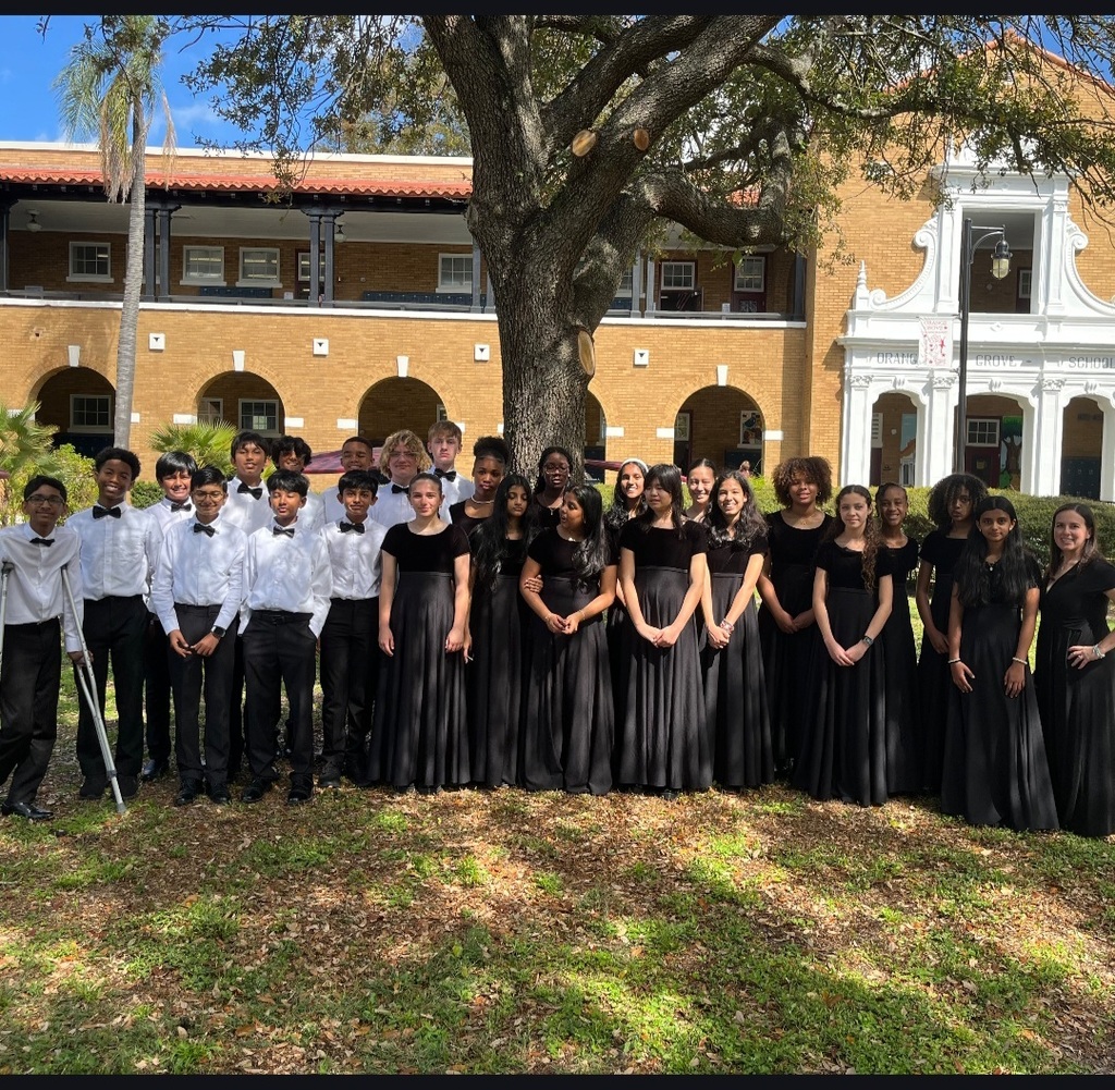 Orchestra students standing in front tree and building.