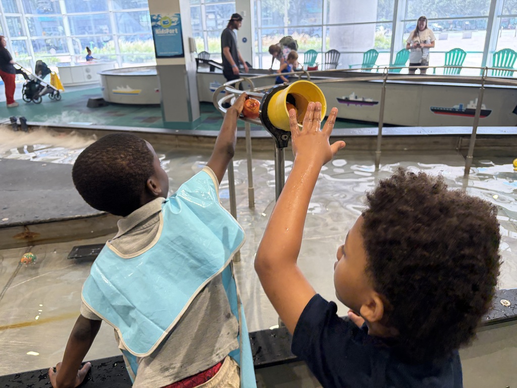 Two young male students playing with a ball and ball chute at the children's museum