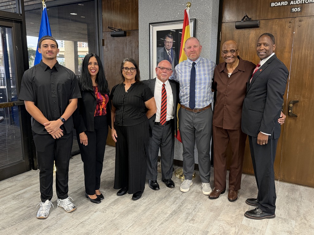Board Members Nadia Combs and Henry "Shake" Washington smiling with Hillsborough Head Football Coach Earl Garcia Jr., his son and grandson, and Hillsborough Principal Kevin Gordon