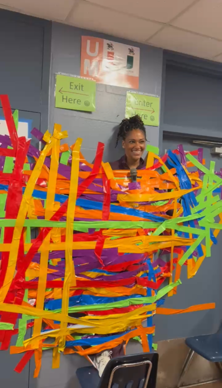 Ms.Webster  taped to the wall with a smile