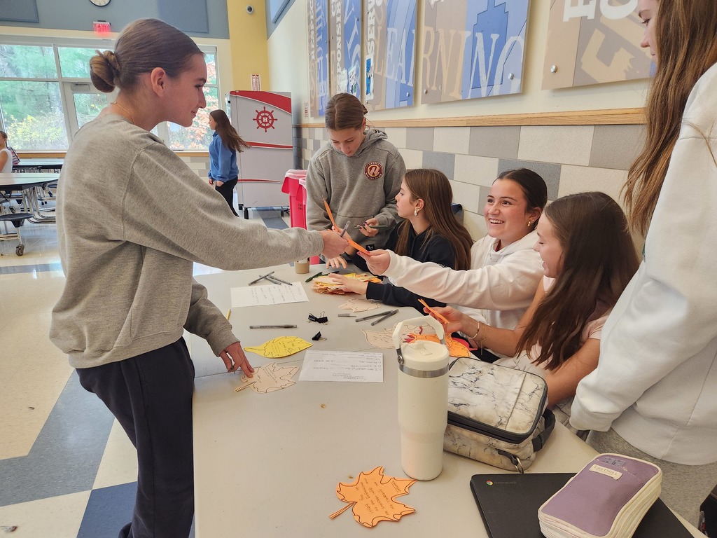 Student handing in a gratefulness leaf to the student council members sitting at a table.
