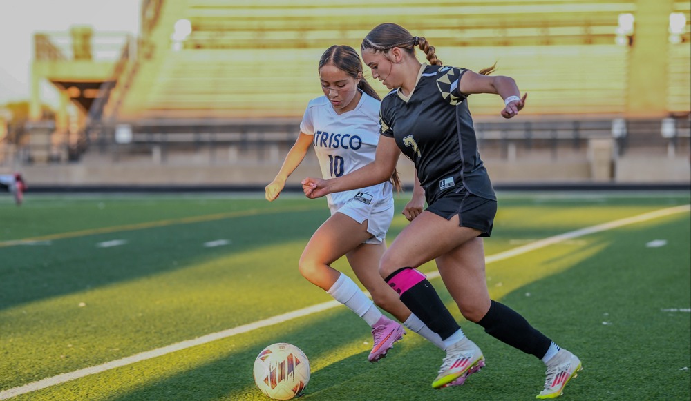 two girl soccer players going for ball