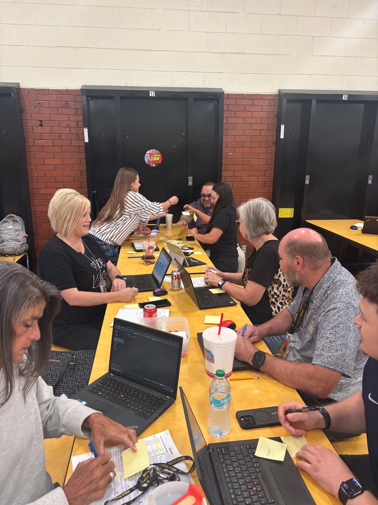 Teachers working at a table with laptops, sticky notes and pens