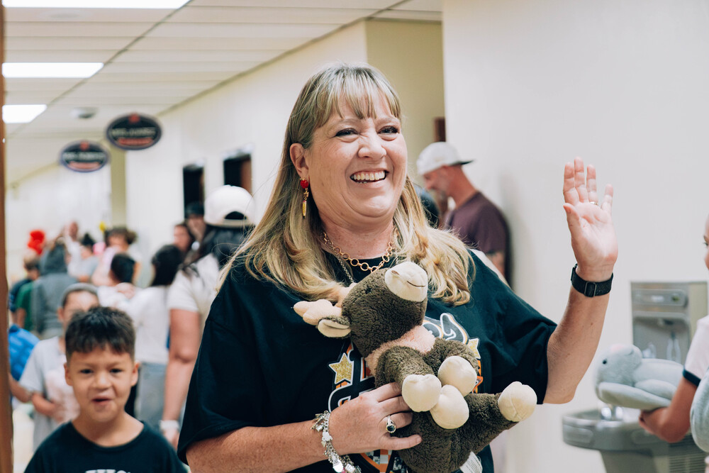 Woman smiles and waves while holding a stuffed animal during the stuffed animal parade.