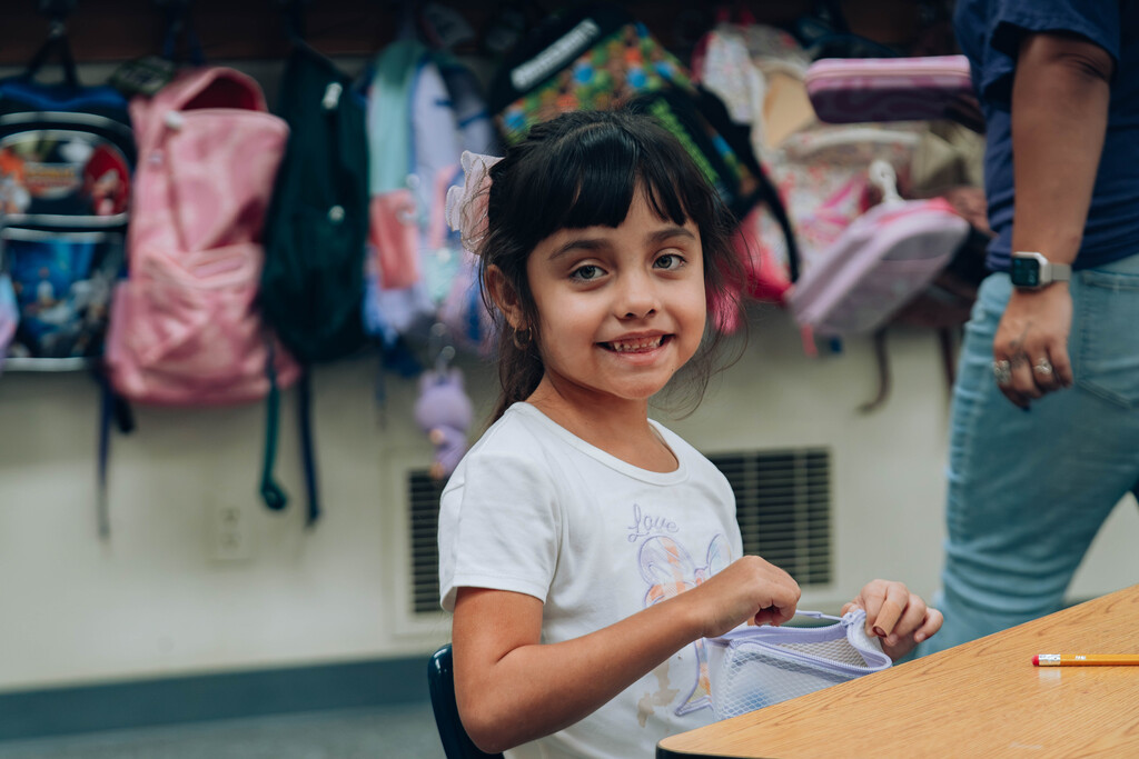 Student smiles in classroom, while gathering supplies. 