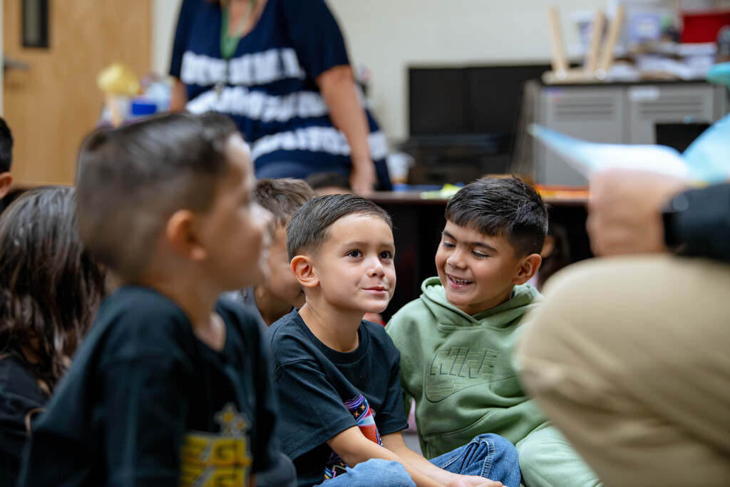 Students smiling and listening as Mr. Strickland reads aloud to the classrom.