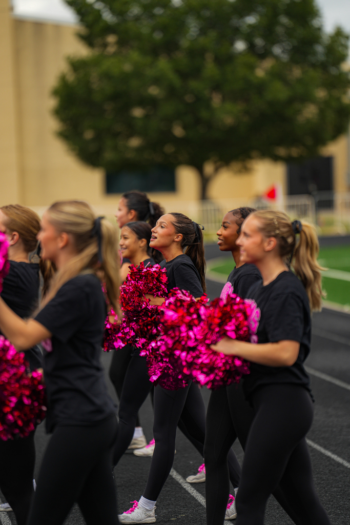 Hobbs Varsity Cheerleaders, shown cheering on the sideline holding pink pom poms in honor of Breast Cancer Awareness Month