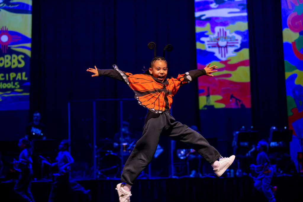 Student wearing butterfly costume excitedly jumps on stage during the NDI performance
