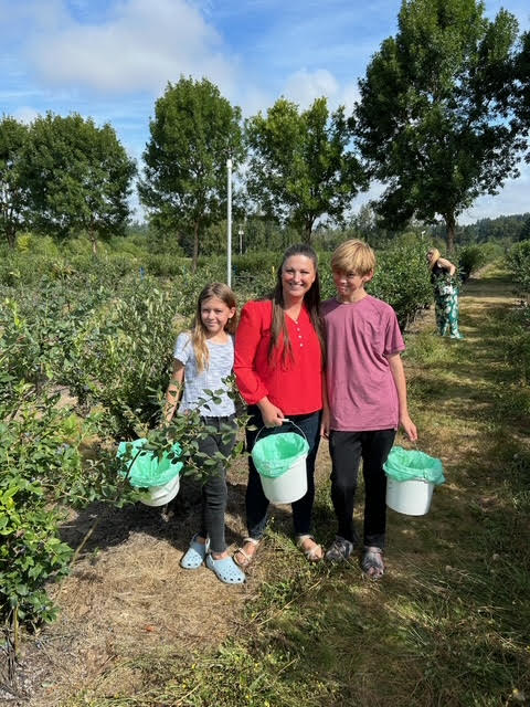 Adult with two children in blueberry field.