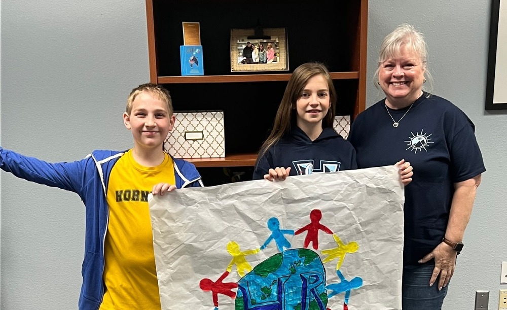 Two middle school students present adult staff member with a painting of a world with people around it.