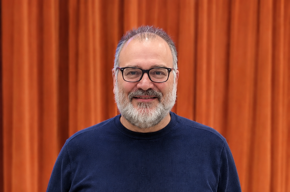 Man smiles as he stands in front of an orange stage curtain.
