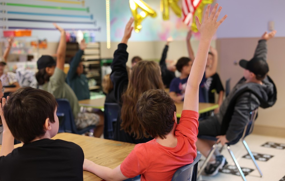 Photo of students in classroom raising their hands