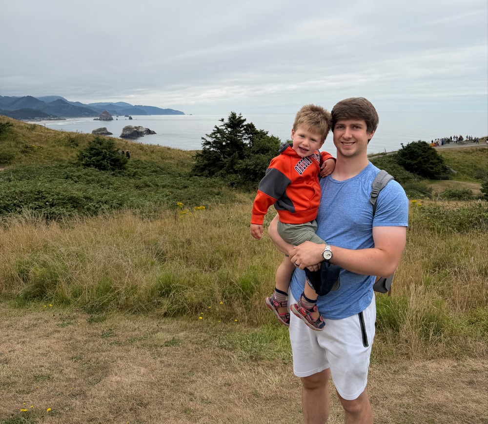 Adult with a young son standing outdoors with Columbia River Gorge in the background.