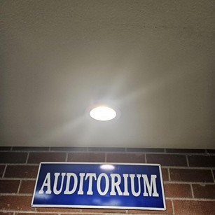 Light fixture on ceiling with auditorium sign on wall.