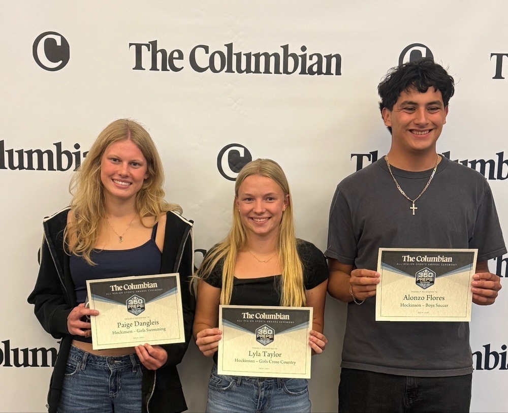 Three students hold certificates with The Columbian name and logo.