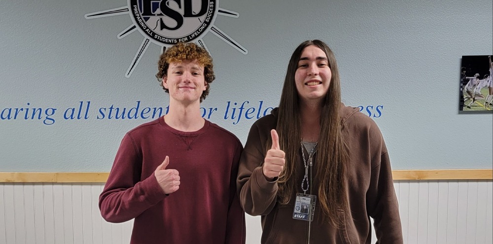 Two adults stand in board room giving thumbs up