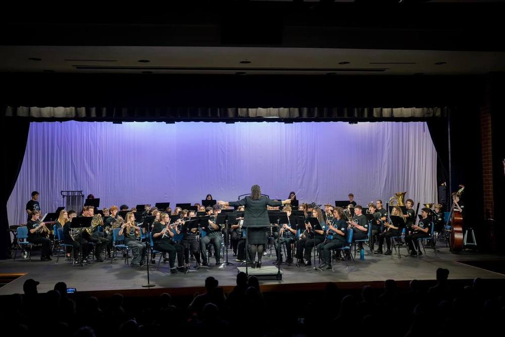 Band with conductor on stage with purple curtains in background.