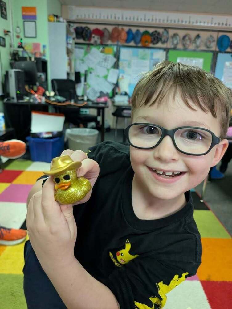 Child holds a golden rubber duck in a classroom.