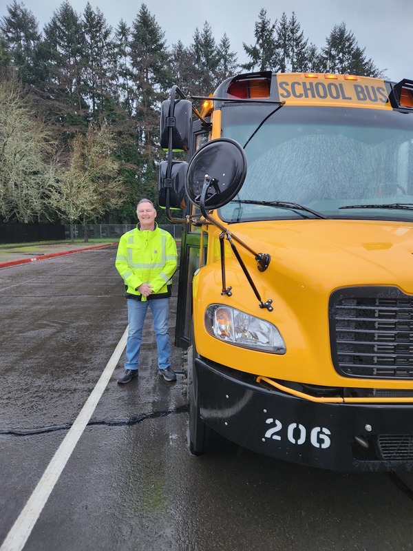 Bus druver stands next to a school bus outdoors