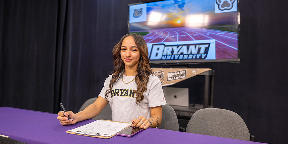 Student sitting at table signing contract to play for Bryant University