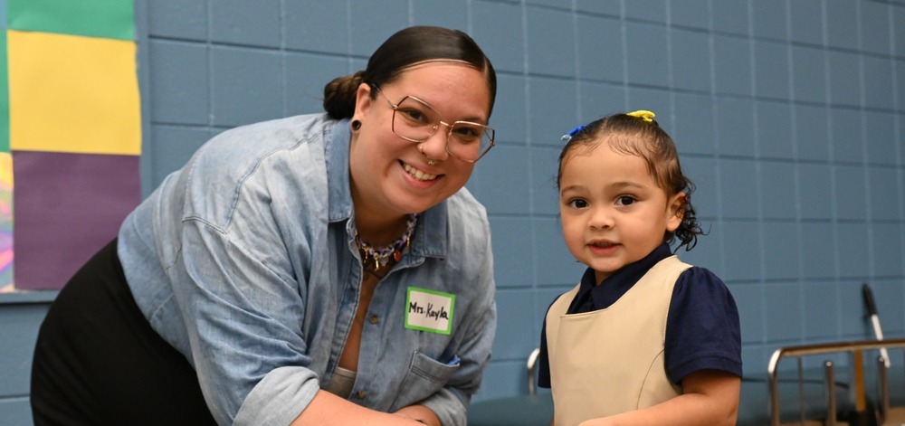 A teacher and PreK student smile at the camera