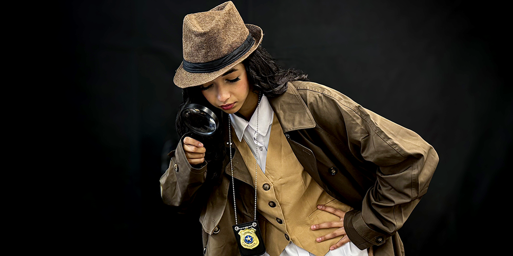 Student wearing detective costume and hat peering through a magnifying glass
