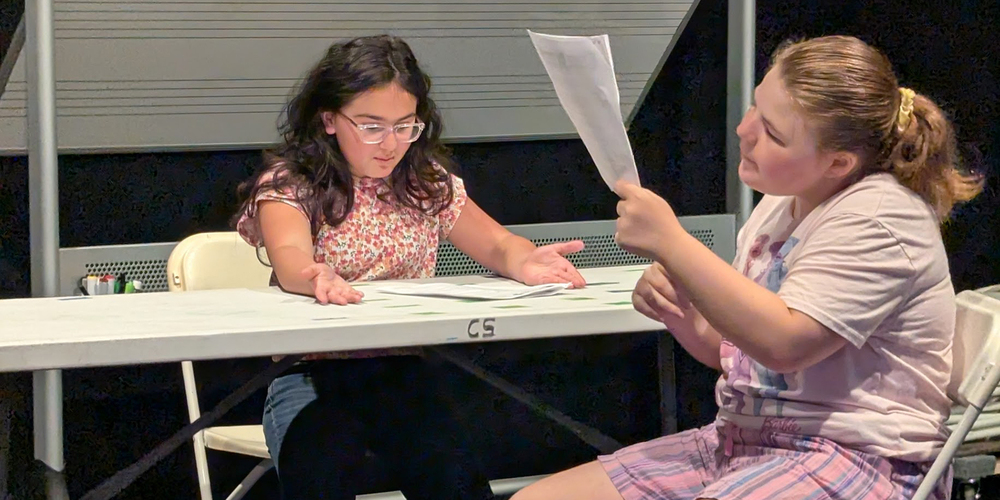 Two students reading a play script at a table