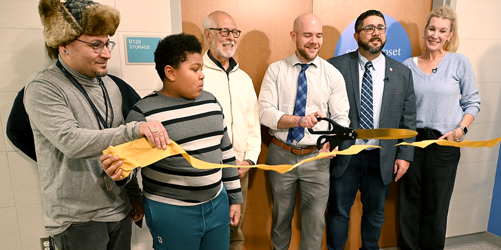 Principal Kevin McGrath cuts a yellow ribbon with a large scissors while four others look on