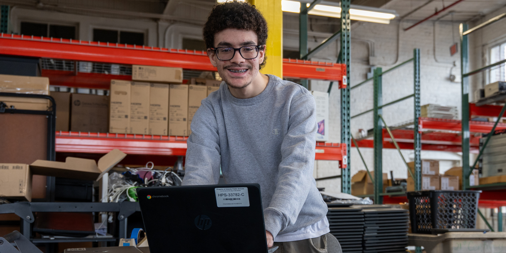 student poses while working on a laptop in IT deparment