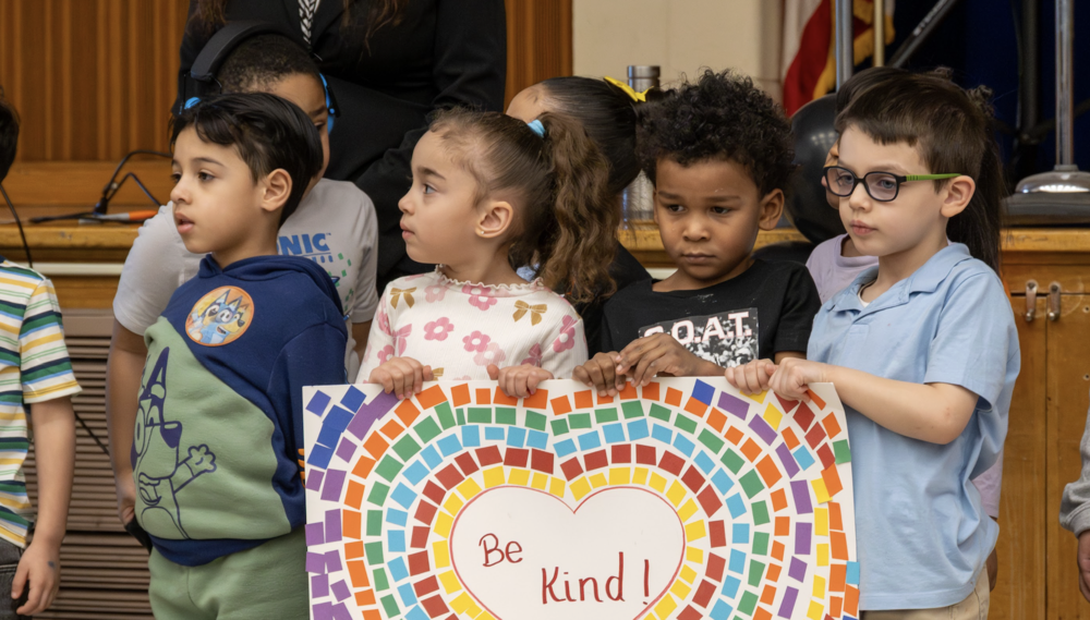 PreK students hold up a sign that says "Be Kind!"