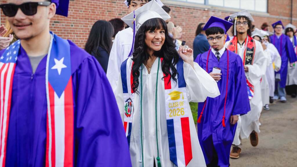 Graduate smiles to camera while walking into graduation