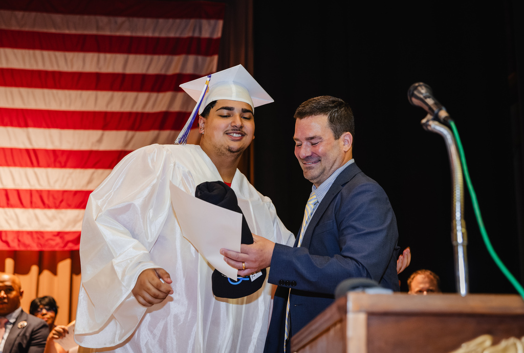 Graduate and teacher smile as he receives his diploma.